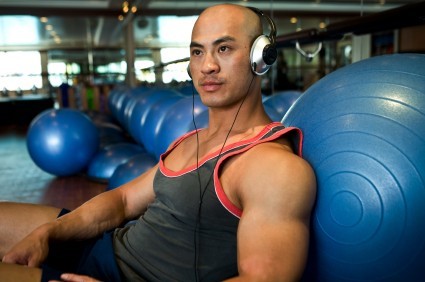 A man leaning against balance balls at the gym listening to music.