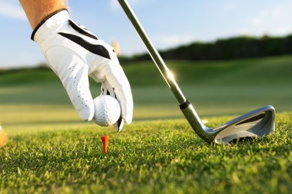 A close up shot of a golf ball being placed on a tee and a golf club.