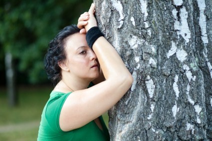 An overweight woman tired from jogging and leaning against a tree.