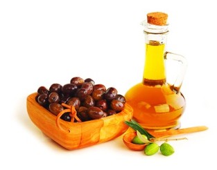 A wooden bowl of black olives next to a bottle of extra virgin olive oil.