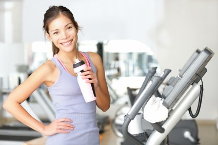 A woman standing on a cardio machine with a bottle of water smiling.