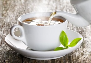 A pot of green tea being poured into a white cup and saucer.