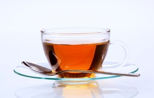 A glass cup of black tea on a glass saucer with a teaspoon.