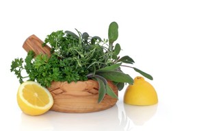 A basket of herbs with 2 lemons on the side.