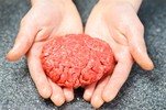 A person holding a home made burger patty in their hand.
