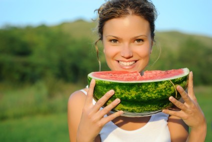 A woman eating a melon in a field.