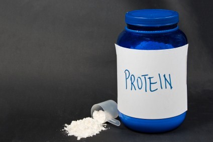A tub of protein powder and a spilled scoop of protein powder.