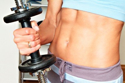 A close up of a woman's abdominals as she holds a dumbbell.