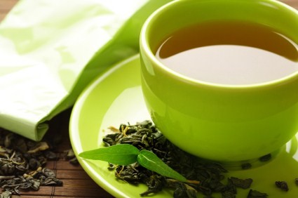 A cup of green tea on a green saucer with green tea leaves.