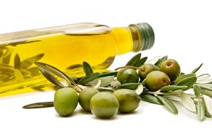 A bottle of olive oil on its side next to a branch of green olives.