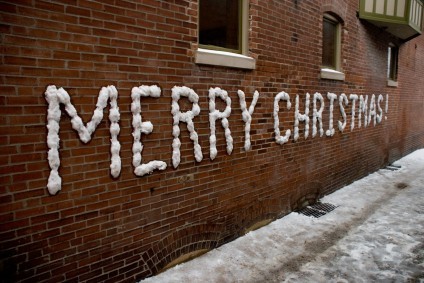 Merry Christmas written in snow on a brick wall.