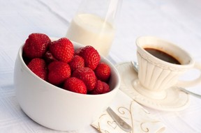 A bowl of strawberries, a jug of cream and a cup of black coffee.