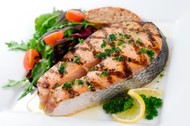 A grilled salmon steak with lemon, tomatoes and parsley.
