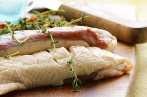 A raw duck breast garnished with herbs and spices.