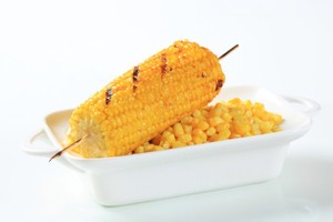 A bowl of corn topped with one piece of corn on the cob.