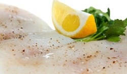 A white fish coated in spice and topped with a lemon wedge and parsley.