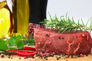 A joint of beef surrounded by black peppercorns and extra virgin olive oil.
