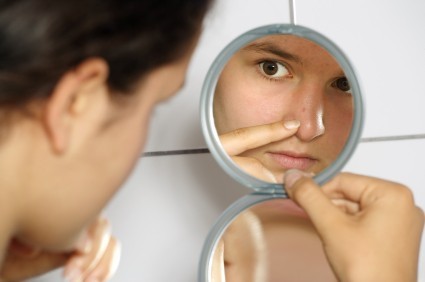 A woman with a spot examining it in the mirror.