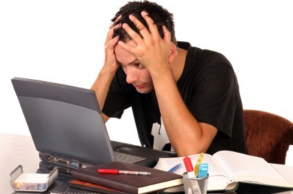 A stressed student with his head in his hands staring at a laptop screen.