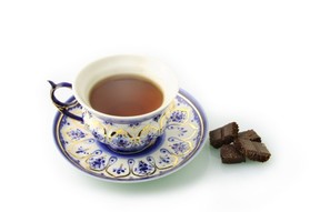 A cup of black tea and a saucer next to some dark chunks of chocolate.