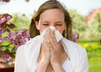 A woman in a field on a summer day, sneezing into a handkerchief.