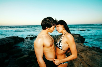 A young couple standing on the rocks near the sea.