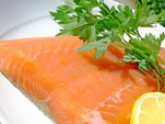 A close up shot of a salmon fillet garnished with lemon and parsley.