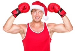 A man in a Santa hat flexing his muscles and wearing boxing gloves.