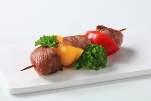 A pork and bell pepper kebab on a white plate.