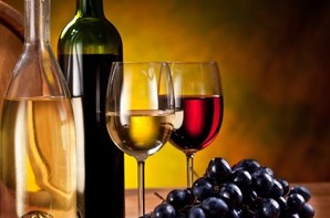 A bottle of wine, 2 glasses of wine and a pile of grapes.