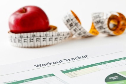 An apple and a tape measure next to a workout tracker sheet.