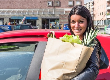 A woman standing next to a car with a bag of groceries.