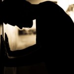 A man with his head and hands against a wall.