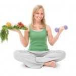 A woman sitting with vegetables in one hand and a dumbbell in the other.
