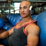 A man leaning against balance balls at the gym listening to music.