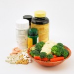A selection of vitamin pills and bottles next to a bowl of fresh vegetables.