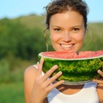 A woman eating a melon in a field.