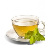 A glass cup of green tea with a leaf next to it.