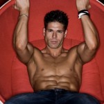 A man with toned abs sitting in a red chair.