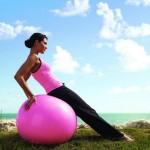 A woman on a pink exercise ball in an empty field.