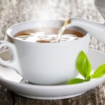 A cup of green tea being poured into a white cup on a saucer.