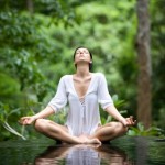 A woman doing yoga in a green forest.