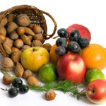 A basket of nuts next to a pile of fruit on a white background.