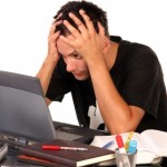 A stressed student with his head in his hands staring at a laptop screen.