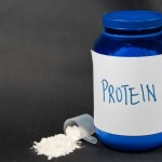 A tub of protein powder and a spilled scoop of protein powder.