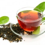A glass cup of black tea surrounded by tea leaves.