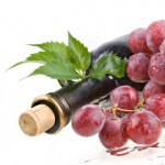 A bottle of red wine surrounded by red grapes.