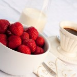 A bowl of strawberries, a jug of cream and a cup of black coffee.