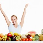 A happy women with her arms raised behind a selection of healthy foods.