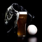 A black baseball glove on top of a pint of beer with a white baseball to the right.